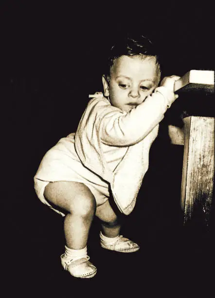 Vintage black and white image of a baby boy trying his first steps.