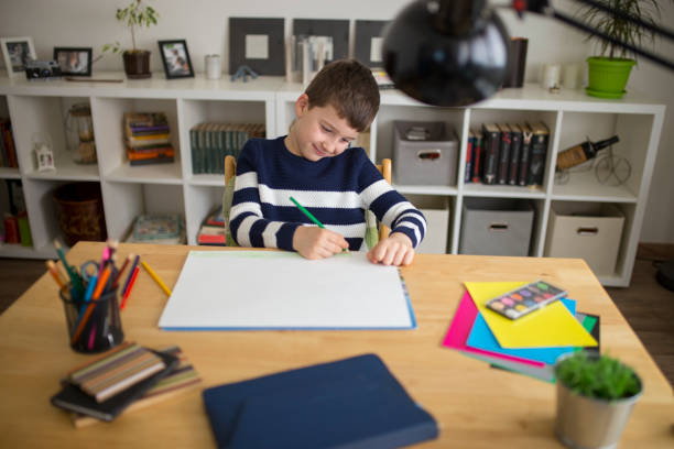 istock Young boy sitting at the table doing his school homework 916960236
