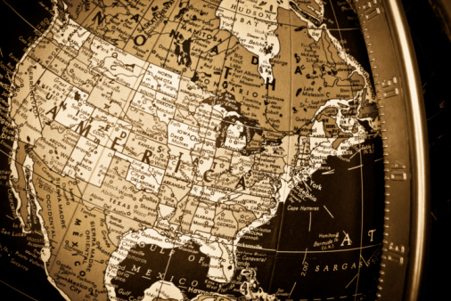 close up of the United States of America on an antique globe. Most of Canada and Mexico is also visible in the image as well as the longitudinal metal bar to the right of the picture. The image is cross-processed to achieve a sepia tone.