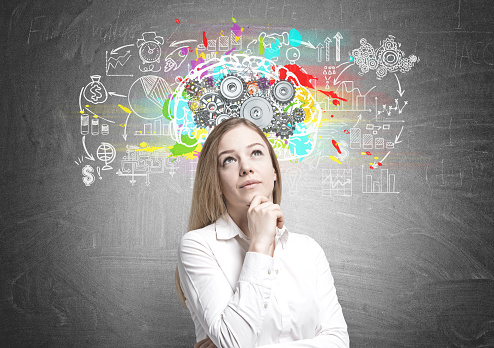 Portrait of a beautiful young businesswoman wearing a white shirt and a skirt and thinking. She is looking upwards. A blackboard with a brain with gears on it. Mock up