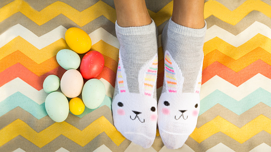 Fun bright and colorful Flat Lay of person wearing bunny socks with Easter eggs on modern Chevron patterned picnic blanket or fabric. Copy space for letters, text, inscription.