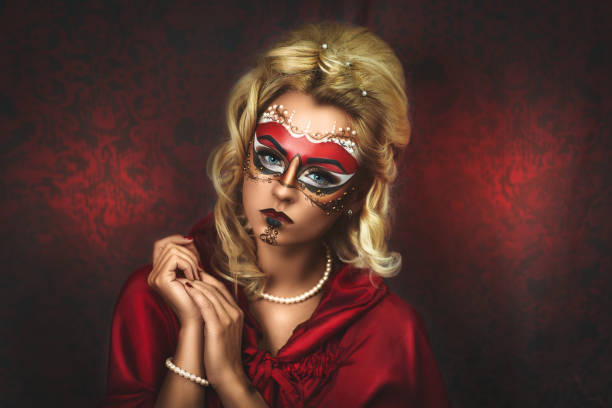 Portrait of beautiful young girl with new creative make up carnival mask, hands near face, blonde hairstyle. Louis court intrigues. Red background. Free place on photo can be used for text inscription