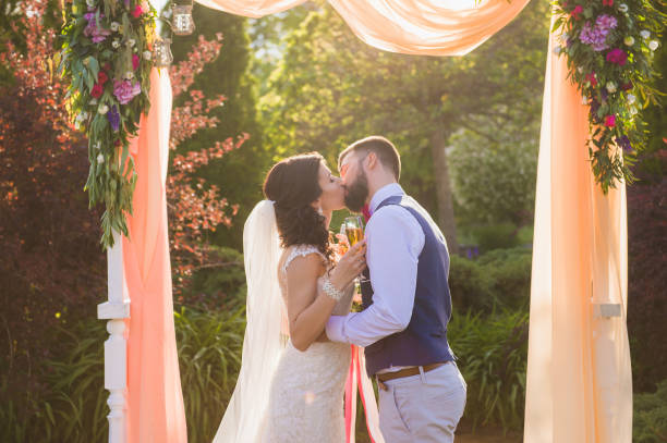 Just married couple in love under arch outdoors Groom and bride have a kiss during their wedding ceremony in the garden country wedding arches stock pictures, royalty-free photos & images