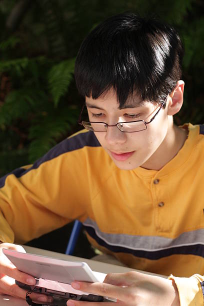 istock Teenage Boy Concentrates on His Hand-Held Gaming Device 91702271