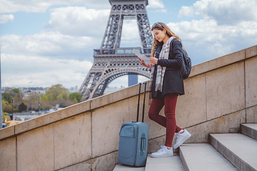 Beautiful young tourist woman near the Eiffel tower in Paris, looking at the city map