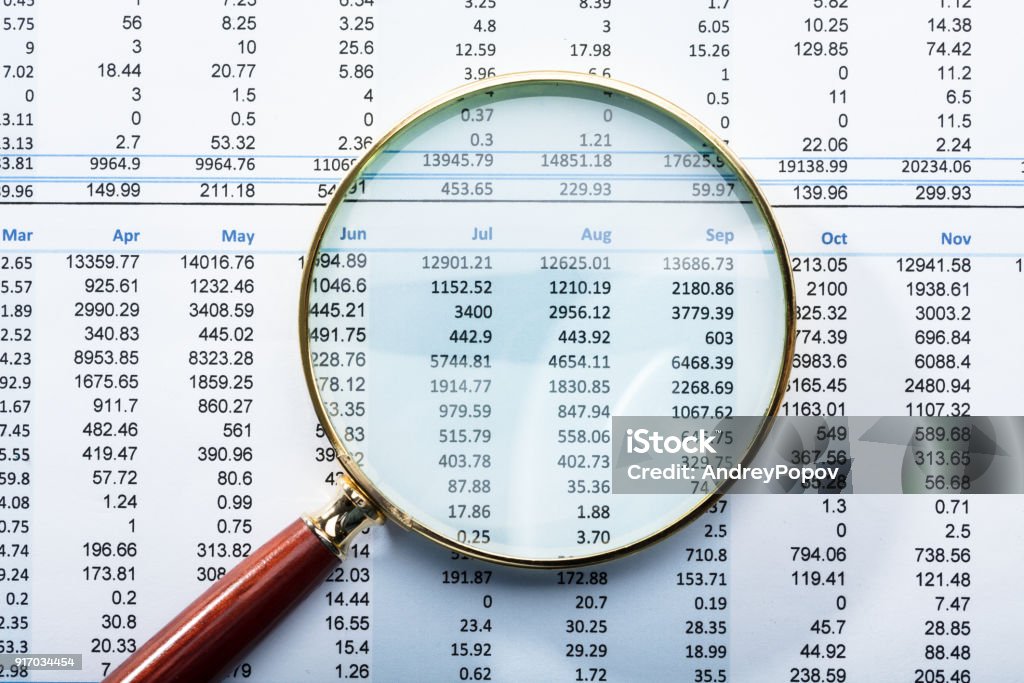 Magnifying Glass On Financial Report Close-up Of Magnifying Glass On Monthly Financial Report Audit Stock Photo