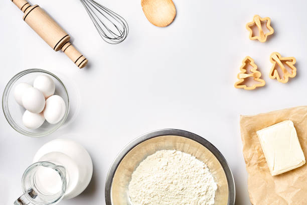 Objects and ingredients for baking, plastic molds for cookies on a white background. Flour, eggs, rolling pin, whisk, milk, butter, cream. Top view, space for text stock photo