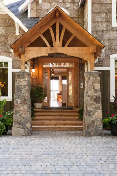 Stone and wood front porch entryway to upscale country house with open front door and paving stone driveway.