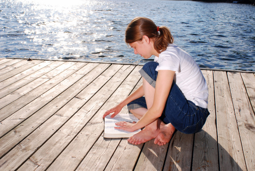 A beautiful young woman prays while studying her Bible outside. 