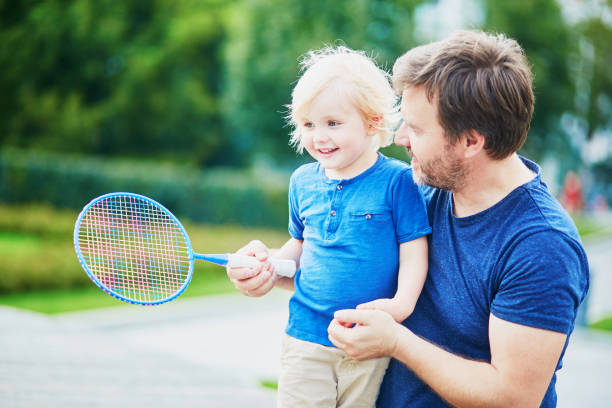 маленький мальчик играет в бадминтон с папой на детской площадке - racquette стоковые фото и изображения