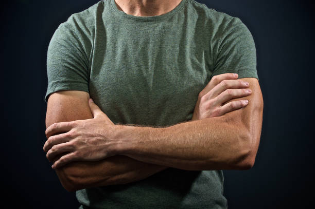 A male's muscular arms folded on his green t-shirt with open hands against a  Dark Background Cape Town South Africa
