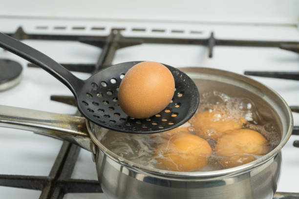 huevos de gallina hervir en agua. la bandeja con el producto en una estufa de gas. - hervido fotografías e imágenes de stock