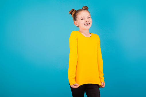 isolated on blue, adorable red-haired girl with freckles in lemon sweater and black trousers, shrugging and looking into the camera. copyspace.