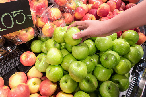 Woman hand choosing apple during shopping at the supermarket.