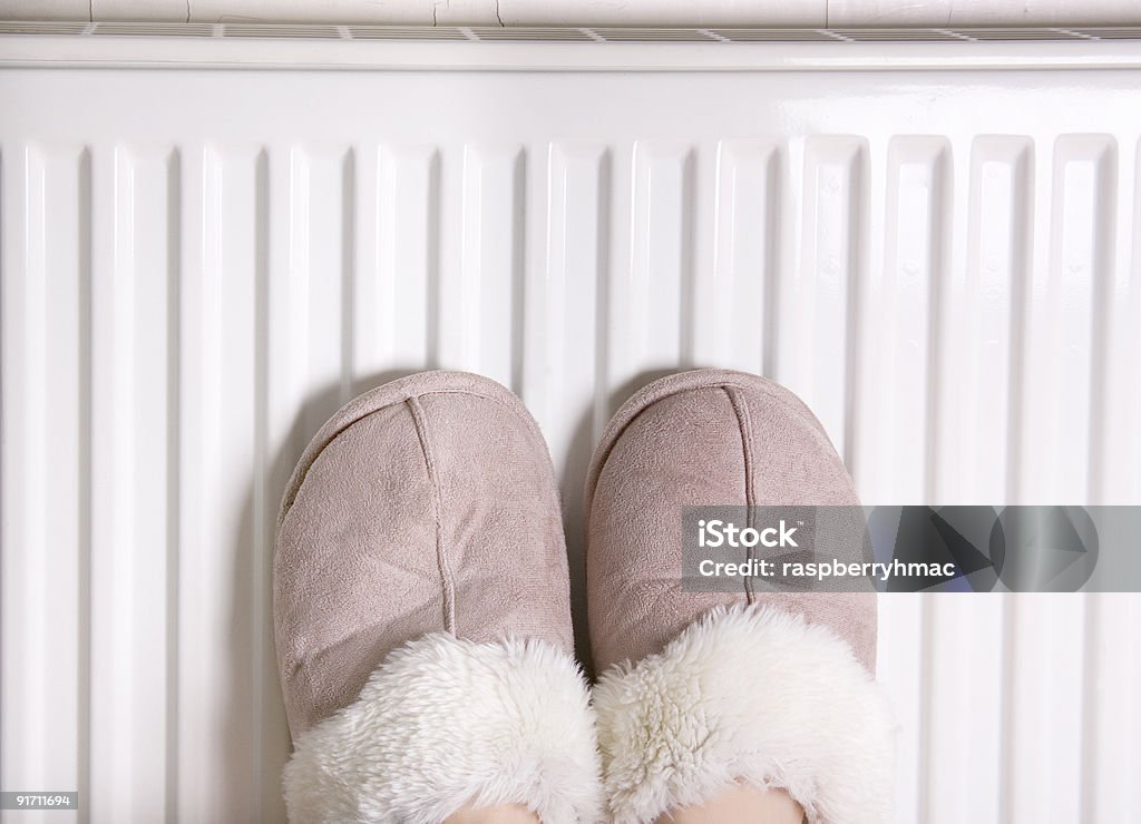 Feet in slippers See my other feet images. Two feet with slippers placed on a heater for warmth, shot landscape Carefree Stock Photo