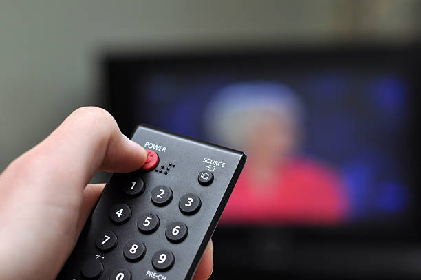 A hand pressing a red power button on a TV remote