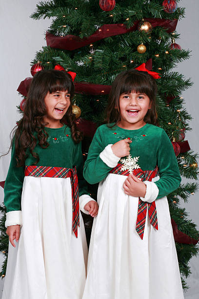 Two Little Sister Girls Dancing by the Christmas Tree. They are celebrating new year and hugging.
