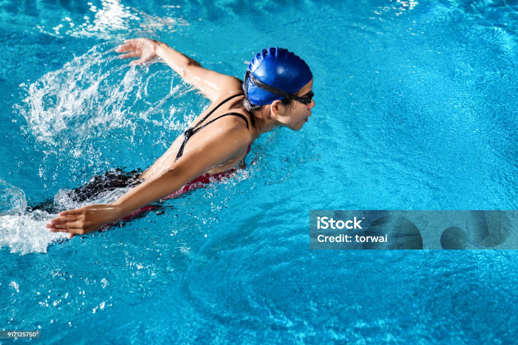 Swimmers are swimming "butterfly" poolside at night. Swimming Stock Photo