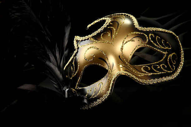 A beautiful carnival mask with black feather and gold decor ornate carnival mask over black silk background evening ball photos stock pictures, royalty-free photos & images