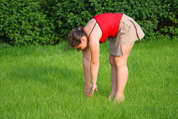 Girl bend forward on grass sideview stock photo