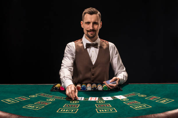 Portrait of a croupier is holding playing cards, gambling chips on table. Black background stock photo