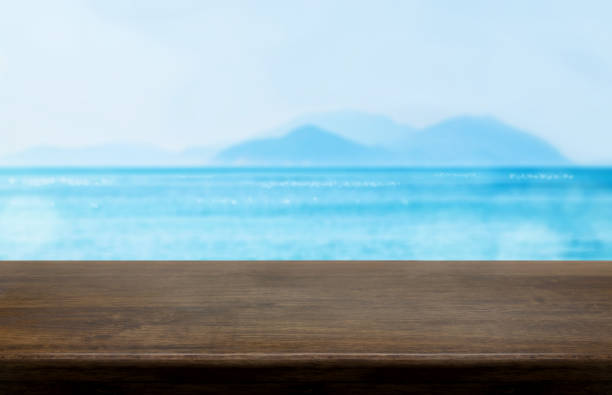 istock Empty old dark wood table top with blur blue sky and sea bokeh background,Mock up template for display or montage of product or content use as banner in social media ads 917159062