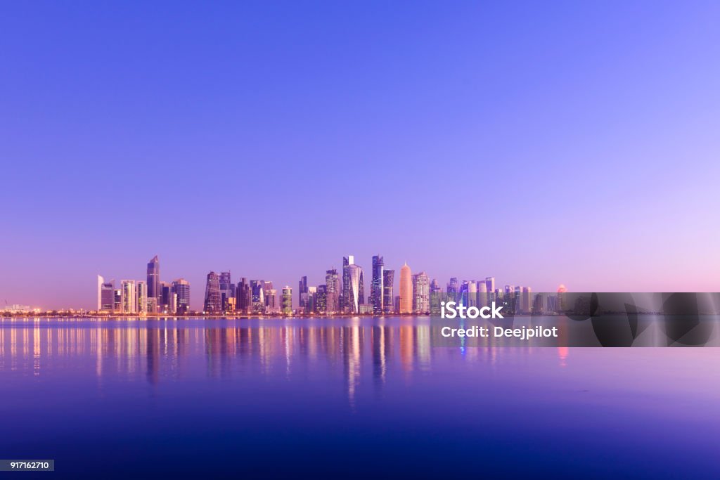 The Downtown Doha City Skyline at Sunset, Qatar Futuristic Modern Skyline with Reflection in the Still Corniche Bay Waters, Last of the Sunlight Falling on the Buildings. Qatar Stock Photo