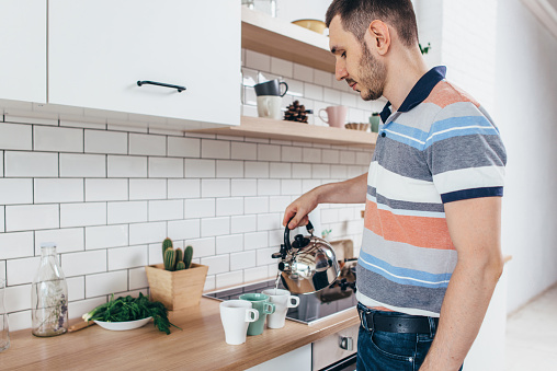 Young man prepare breakfast with tea pour water from kettle in kitchen