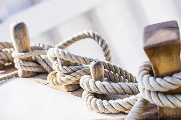 Photo of Old sailboat, detail closeup of wooden cleats with nautical moored ropes