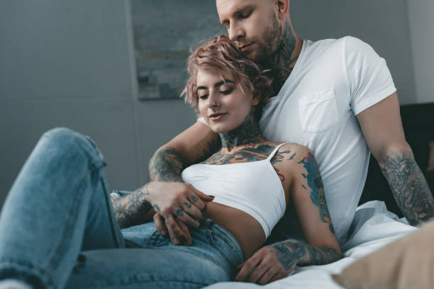istock tender tattooed couple hugging, holding hands and lying on bed 917205894