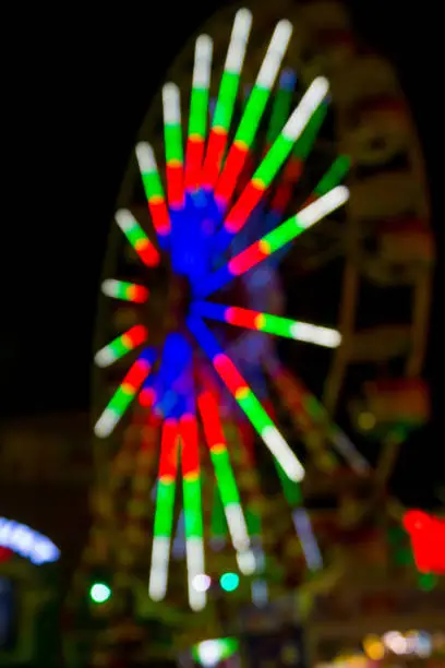 neon lights on ferris wheel in amusement park, night blurred shot