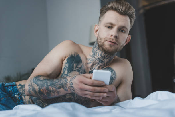 istock handsome shirtless tattooed man using smartphone on bed 917210452