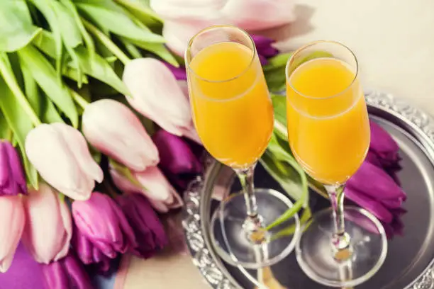 Two glasses of mimosa cocktail (champagne with orange juice) and tulips