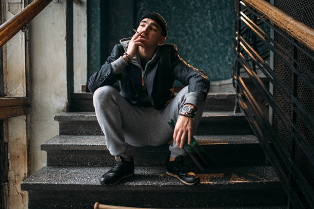 istock Guy with bottle sits on the stairs and smoking 917218128