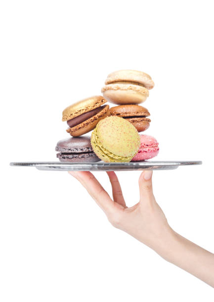 Hand holds tray with sweet macarons dessert cakes on white background with sugar on top