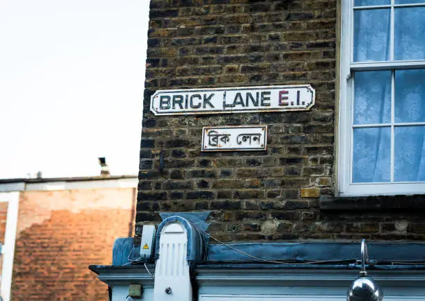 Close up color image depicting the Brick Lane street in sign on a brick wall in east London, UK. Beneath the sign, a separate sign is also displayed in Urdu, due to the large Asian population in this area of the city. Today, Brick Lane is the heart of the city's Bangladeshi-Sylheti community and is known to some as Banglatown. It is famous for its many curry houses. Room for copy space.