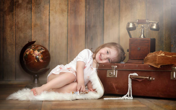 A child in a retro interior and an old phone sits on the floor. A small child a traveler in vintage decorations. Child traveler is calling by phone.