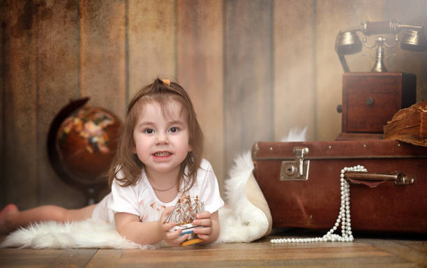 A child in a retro interior and an old phone sits on the floor. A small child a traveler in vintage decorations. Child traveler is calling by phone.