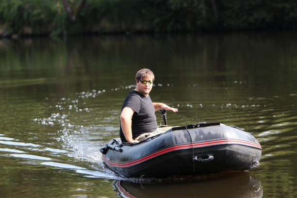 Young man in inflatable boat Young man in inflatable boat with electric outboard driving on river. freshwater fishing photos stock pictures, royalty-free photos & images