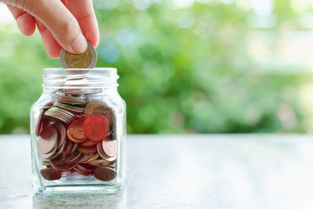 istock Hand saving a coin into the glass jar on blurred green natural background with copy space for business and finance concept 917233568