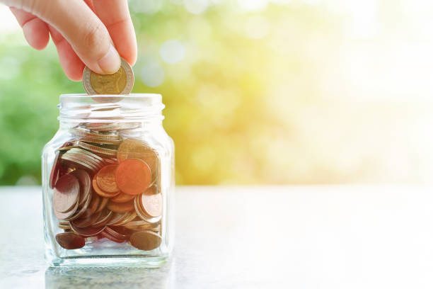 istock Hand saving a coin into the glass jar on blurred green natural background with sun light effect and copy space for business and finance concept 917233708