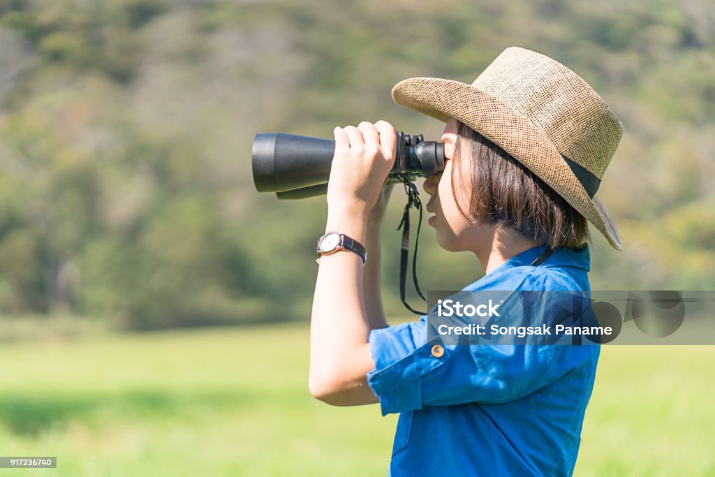 young teenager wear hat and hold binocular in grass field Young asian teenagershort hair wear hat and hold binocular in grass field countryside Thailand 14-15 Years Stock Photo