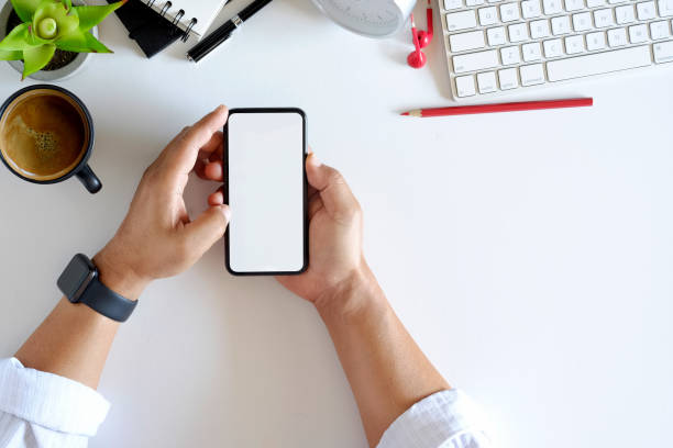 istock Male hands using smartphone mockup at the white office desk. Blank screen mobile phone for graphic display montage 917236762