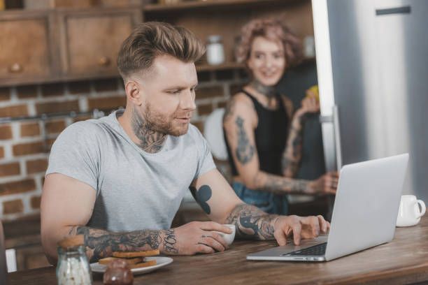 istock tattooed man using laptop during breakfast, girlfriend behind in kitchen 917245712