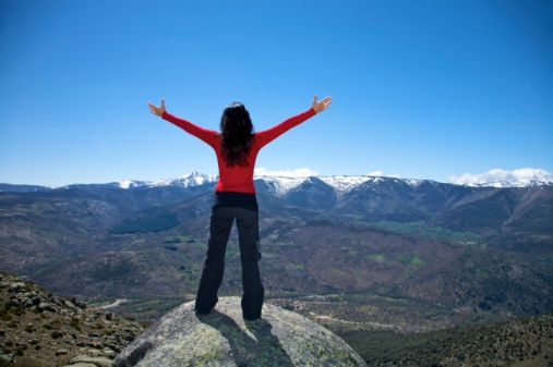 young back brunette woman red sweater black trousers standing with open arms greeting nature like flying at the top of summit in Gredos mountains Avila Spain Europe with copy space blue sky