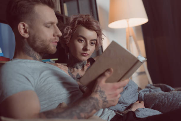 istock tattooed couple reading book while lying on sofa at home 917246856