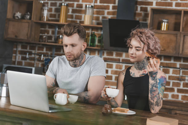 istock tattooed couple using laptop and eating toasts for breakfast in kitchen 917250692