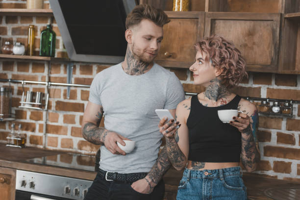 istock young tattooed couple drinking coffee and using smartphone in kitchen at morning 917251226