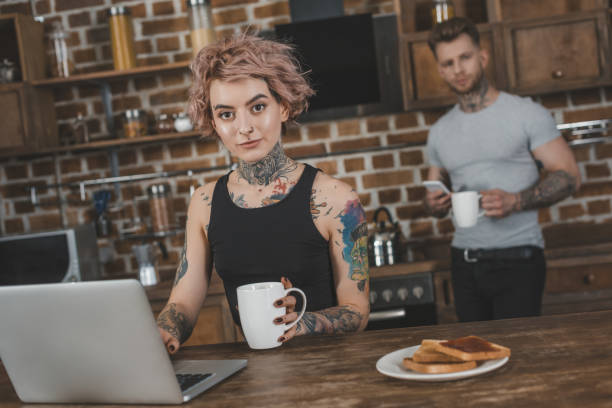 istock tattooed girl using laptop during breakfast, boyfriend behind in kitchen 917251532