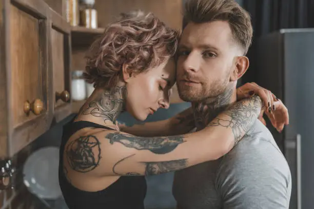 Photo of young tattooed couple embracing in kitchen